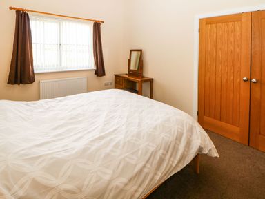 A bedroom with a bed a window with curtains a wooden dressing table with mirror and wooden doors at Coquet in Longframlington near Alnwick