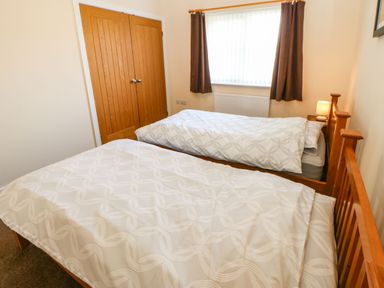 A bedroom with two single beds a window with curtains a wooden closet and a bedside table with a lamp at Coquet in Longframlington near Alnwick