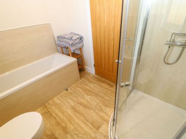 A bathroom with a bathtub towels on a wooden shelf a wooden door a shower with glass doors and a toilet at Coquet in Longframlington near Alnwick
