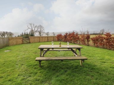 A wooden picnic table with a bottle and two glasses on grass in a fenced backyard at Coquet in Longframlington near Alnwick