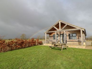A wooden cabin with a porch and picnic table on a green lawn with a rainbow in the background at Coquet in Longframlington near Alnwick