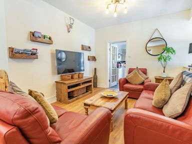 A living room with red leather sofas a wooden coffee table a wall-mounted tv and a round mirror at Dringarth in Tenby