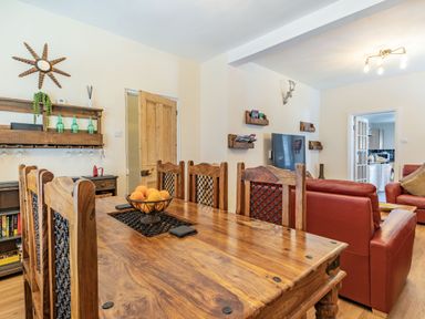 A dining area with a wooden table and chairs and a living room with red sofas and a TV at Dringarth in Tenby