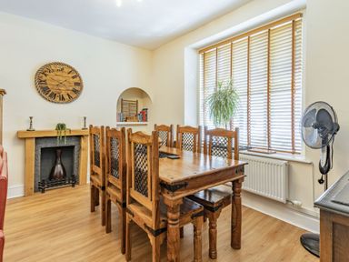 A dining room with a wooden table and chairs a large window with wooden blinds and a clock on the wall at Dringarth in Tenby