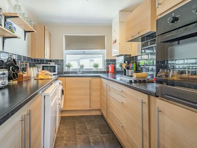 A kitchen with wooden cabinets black countertops a window with a roller blind and various kitchen appliances at Dringarth in Tenby