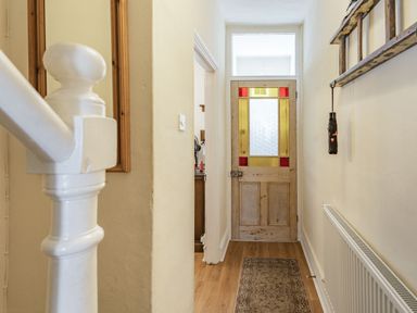 A narrow hallway with a wooden floor radiator and a door with yellow and red stained glass at Dringarth in Tenby
