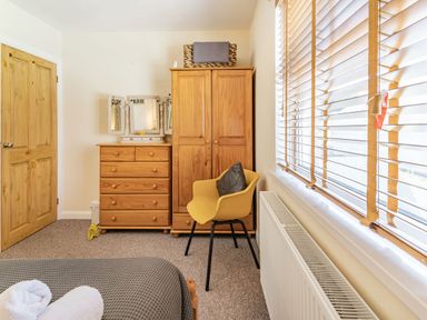 A bedroom with wooden wardrobe chest of drawers yellow chair and window blinds at Dringarth in Tenby