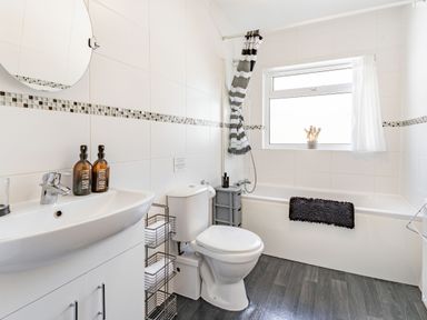 A bathroom with a sink cabinet and mirror a toilet a bathtub with shower curtain and window at Dringarth in Tenby