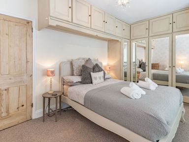 A bedroom with a double bed cushions bedside table lamps wooden door and built in wardrobes with mirrored doors at Dringarth in Tenby