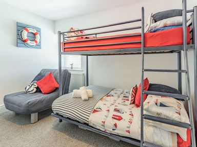 A bedroom with a bunk bed and a grey chair with cushions at Dringarth in Tenby
