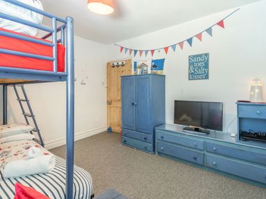 A bedroom with blue bunk beds a wooden door blue wardrobe and blue dresser with a television and nautical decorations at Dringarth in Tenby
