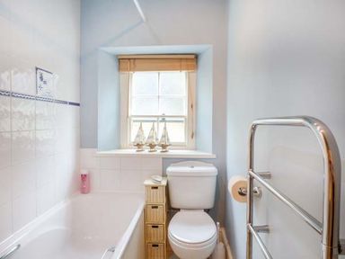 A bathroom with a bathtub toilet small storage unit and window at Cobble Cottage in Boscastle near Tintagel