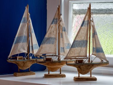 Three model sailboats with blue and white sails on a white windowsill at Cobble Cottage in Boscastle near Tintagel