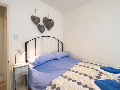 A bedroom with a double bed blue bedding quilt bedside table lamp and heart-shaped wall decor at Cobble Cottage in Boscastle near Tintagel