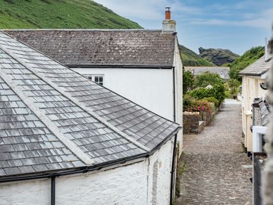 A narrow cobblestone street between white buildings with slate roofs and a green hill in the background at Cobble Cottage Boscastle near Tintagel