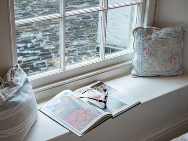 A window seat with an open book and sunglasses between two cushions at Cobble Cottage in Boscastle near Tintagel