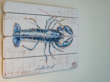 A wall art piece of a blue lobster painted on three wooden panels at Cobble Cottage in Boscastle near Tintagel