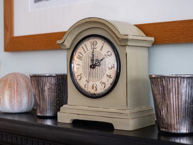 A mantel clock with decorative cups and a sea urchin shell on a shelf at Cobble Cottage in Boscastle near Tintagel