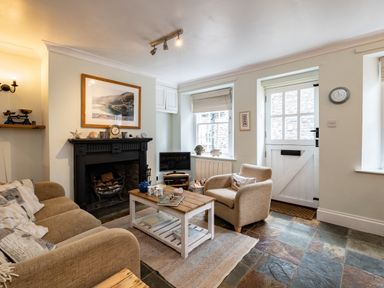 A living room with a beige sofa and armchair a wooden coffee table a black fireplace and a white door at Cobble Cottage in Boscastle near Tintagel