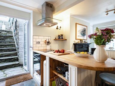 A kitchen with a wooden countertop vase of flowers open door leading to stone stairs at Cobble Cottage Boscastle near Tintagel
