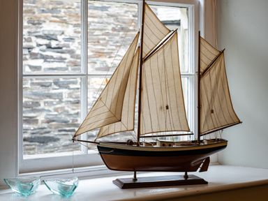 A model sailboat with brown sails on a windowsill with two glass candle holders at Cobble Cottage in Boscastle near Tintagel