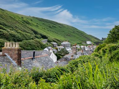 A village with slate rooftops and chimneys surrounded by green hills and vegetation at Cobble Cottage in Boscastle near Tintagel