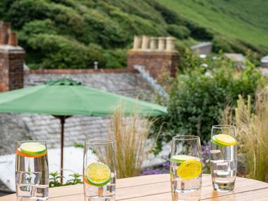 Four glasses of water with lemon and lime slices on a wooden table outside with greenery and rooftops in the background at Cobble Cottage in Boscastle near Tintagel