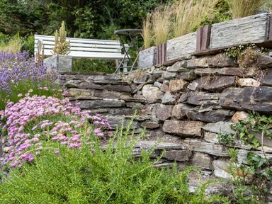 A stone garden terrace with pink flowers a white bench and a folding table at Cobble Cottage in Boscastle near Tintagel