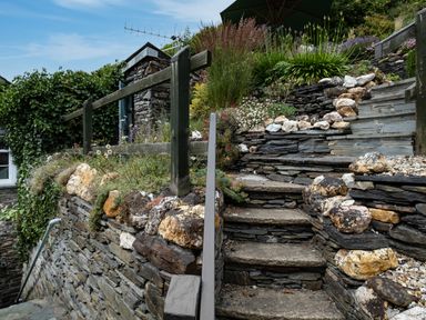 Stone steps with rock and plant bordered retaining walls and wooden railing in a garden at Cobble Cottage in Boscastle near Tintagel