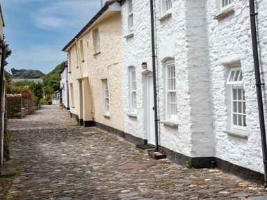 A cobblestone street lined with white and beige stone houses with windows and doors at Cobble Cottage in Boscastle near Tintagel