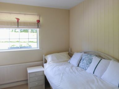 A bedroom with a bed with pillows and a small white bedside cabinet next to a window at Woodbine Cottage in Old Leighlin near Kilkenny County Kilkenny