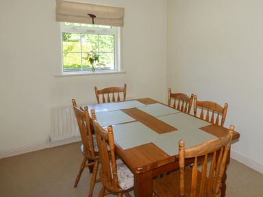 A dining room with a wooden table and six chairs and a window with a flower vase at Woodbine Cottage Old Leighlin near Kilkenny County Kilkenny