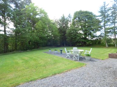 A garden with a gravel path a round table and four chairs and potted plants surrounded by trees at Woodbine Cottage in Old Leighlin near Kilkenny County Kilkenny