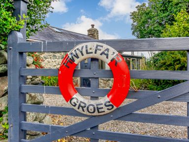 A wooden gate with a life ring attached and a stone building with plants behind at Hwylfa'r Groes in Talybont near Barmouth