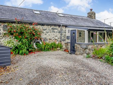 Exterior of a stone cottage with a gravel driveway and plants near the entrance at Hwylfa'r Groes in Talybont near Barmouth
