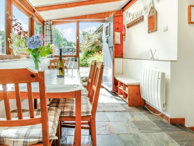 A dining area with wooden chairs and a table with a bottle and glasses near an open door at Hwylfa'r Groes in Talybont near Barmouth