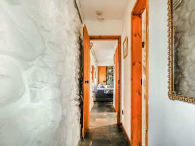 A hallway with a stone wall and wooden door frames leading to a living room at Hwylfa'r Groes in Talybont near Barmouth
