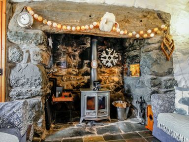 A stone fireplace with a wood stove and decorative lights in a living room at Hwylfa'r Groes in Talybont near Barmouth