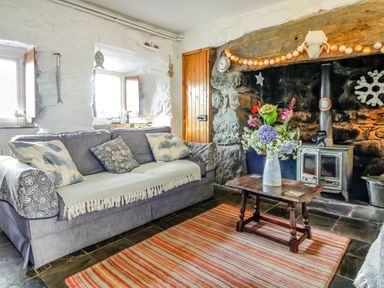 A living room with a grey sofa a wooden coffee table with flowers and a wood stove at Hwylfa'r Groes in Talybont near Barmouth