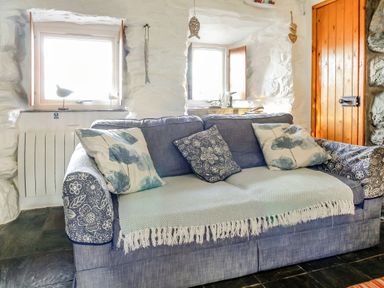 A blue sofa with patterned cushions in front of two windows and a wooden door at Hwylfa'r Groes in Talybont near Barmouth