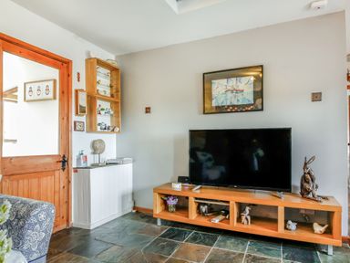 A living room with a television on a wooden stand and decorative items on shelves at Hwylfa'r Groes in Talybont near Barmouth