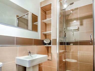 A bathroom with a wall-mounted sink a mirror shelves and a glass shower enclosure at Hwylfa'r Groes in Talybont near Barmouth