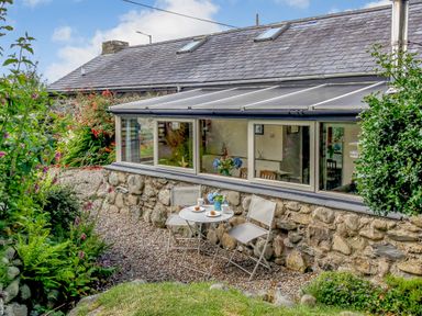 An outdoor seating area with two chairs and a small round table with cups and plates beside a stone cottage at Hwylfa'r Groes Talybont near Barmouth