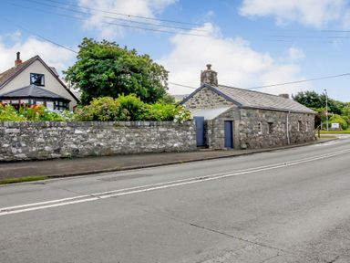 A stone cottage with blue doors beside a flower garden and a road at Hwylfa'r Groes in Talybont near Barmouth