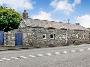 A stone cottage with blue doors and windows beside a road at Hwylfa'r Groes in Talybont near Barmouth