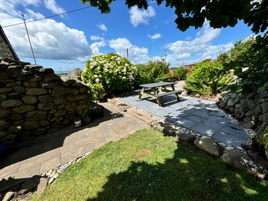 An outdoor garden area with stone walls a picnic table on a paved section and various plants and flowers at Hwylfa'r Groes in Talybont near Barmouth