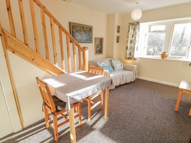 A living room with a wooden dining table and chairs near stairs and a sofa by a window at Bryn Melyn Artist's Cottage Llanelltyd near Dolgellau