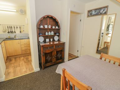 A dining area with a wooden table and chairs next to a kitchen with hanging utensils and a dark wooden cabinet at Bryn Melyn Artist's Cottage Llanelltyd near Dolgellau