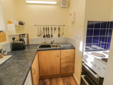 A compact kitchen with a sink utensils on a rack toaster cutting boards and an electric stove at Bryn Melyn Artist's Cottage Llanelltyd near Dolgellau