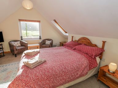 A bedroom with a double bed a bedside table with a lamp two armchairs a small table a window and a skylight at Bryn Melyn Artists Cottage Llanelltyd near Dolgellau